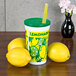 A 16 oz. plastic lemonade cup with a green lid and straw next to lemons.