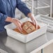 A person in gloves holding a loaf of bread in a white plastic container.