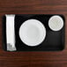 A black rectangular Cambro tray with a white plate and a cup on it.