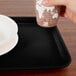 A hand holding a cup over a Cambro black rectangular fiberglass tray.