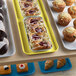 A yellow Cambro market tray filled with pastries and muffins on a bakery display counter.