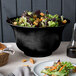 A Tablecraft black cast aluminum tulip salad bowl filled with salad on a table.