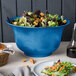 A Tablecraft sky blue cast aluminum tulip salad bowl filled with salad on a table.