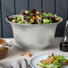 A Tablecraft gray cast aluminum tulip salad bowl filled with salad on a table.