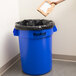 A hand throws a cardboard box into a Continental blue round trash can.