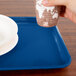 A hand holding a paper cup over a blue Cambro tray.