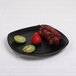 A black Elite Global Solutions square melamine plate with a kiwi on it.