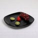 A black Elite Global Solutions square melamine plate with a kiwi on it.