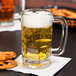 A close up of an Anchor Hocking beer mug filled with beer and pretzels.