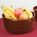 A Tablecraft copper cast aluminum bowl filled with bananas and apples on a hotel buffet table.