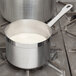 A Vollrath stainless steel sauce pan with a white liquid in it on a stove.