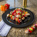 A Carlisle black melamine platter with skewers of peppers and onions on a table.