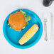 A turquoise blue Creative Converting paper plate with a burger and corn on it.