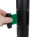 A hand holding a black Aarco crowd control stanchion with dual green belts.