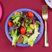 A purple Creative Converting paper plate with a salad, fork, and knife on a table.