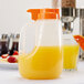 A Tablecraft plastic jug with orange liquid and an orange top next to a glass of orange juice.