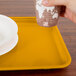 A hand holding a cup over a yellow rectangular tray.
