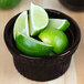 A Tablecraft black cast aluminum bowl with limes and lime wedges inside.
