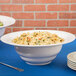A Tablecraft white cast aluminum salad bowl filled with pasta and salad on a blue table.