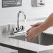 A person washing their hands under a Regency deck mount faucet with a swivel gooseneck spout.