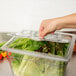 A hand using a Cambro 20CWL135 FlipLid to pick up a salad from a plastic container of lettuce.