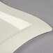 A close up of a Fineline bone/ivory plastic square plate with a curved edge.