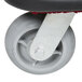A close-up of a rectangular stainless steel luggage cart wheel with a red rubber pad.