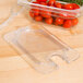 A Carlisle clear plastic food pan lid with a spoon notch on a plastic container with tomatoes.