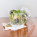A Dart clear plastic container filled with salad with a plastic fork and spoon.