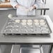 A woman in a white uniform using a Chicago Metallic clustered ePAN to bake pastries.