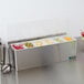 A stainless steel San Jamar condiment bar with different colored food items inside.