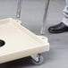 A person using a Vollrath dolly handle to move a wheeled cart with a white tray on it.