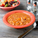 A bowl of soup and a bowl of salad in GET Rio Orange melamine bowls on a wood surface.