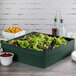 A green Tablecraft cast aluminum square bowl filled with salad on a wood surface.