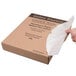 A hand holding a white Baker's Mark parchment paper sheet in front of a brown box.