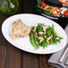 A Carlisle white rimmed oval platter with green beans and chicken on a table.