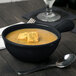 A Tablecraft black cast aluminum soup bowl with croutons and a spoon.