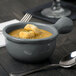 A Tablecraft granite cast aluminum soup bowl with a handle filled with soup and croutons with a spoon on the table.