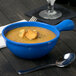 A Tablecraft blue speckle cast aluminum soup bowl with a handle filled with soup and croutons on a table with a spoon.