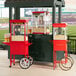 A red Carnival King popcorn cart with a red umbrella on wheels.
