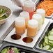 A Tablecraft squeeze bottle holder with eight white containers of sauce on a salad bar.