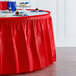 A table with a Classic Red Plastic Table Skirt with cupcakes on it.
