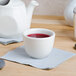 A white Tuxton China sake cup filled with red liquid on a napkin.