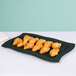 A black rectangular Tablecraft tray with green speckles holding croissants on a white surface.