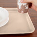 A hand holding a paper cup over a light peach rectangular tray with a plate on it.