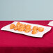 A white Tablecraft cast aluminum rectangular platter with croissants on it on a table with a red tablecloth.