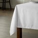 A wooden table with a white Intedge square tablecloth on it.
