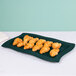 A Hunter green rectangular metal platter holding croissants and a white napkin on a table.