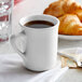 A white Tuxton Concentrix mug filled with brown liquid on a table with croissants.