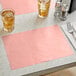 A dusty rose colored scalloped paper placemat on a table with glasses of liquid.